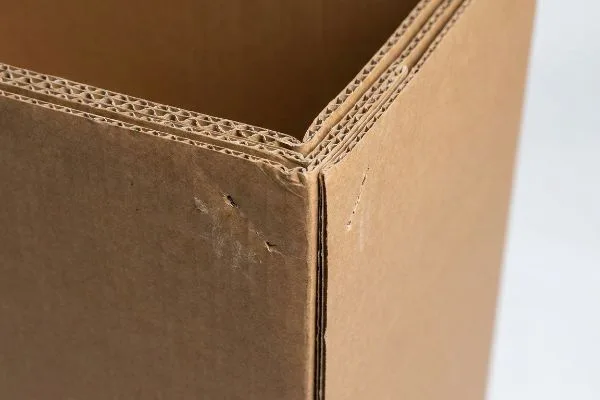 Gros plan sur un coin de boîte en carton ondulé double paroi marron, mettant en évidence ses cannelures visibles et son intégrité structurelle.