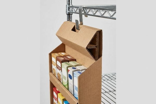 Brown corrugated side kick display, reinforced double-wall header, metal S-clip on wire rack, holding colorful product boxes.