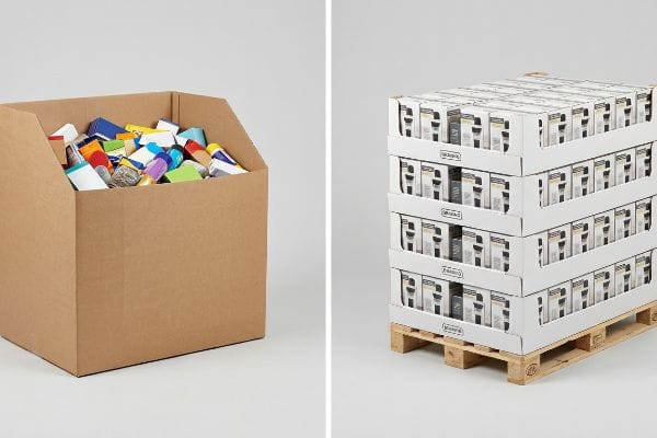 Dans un espace de vente au détail, on aperçoit un conteneur en carton ondulé brun contenant des articles en vrac colorés, à côté d'un présentoir à palettes blanches sur un socle en bois.
