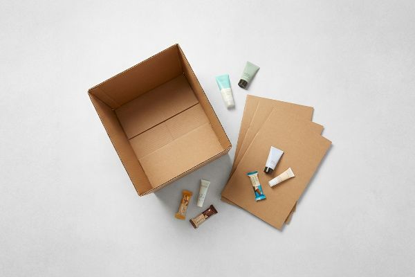 Arranged for bulk merchandising, travel-sized cosmetics and wrapped snack bars sit by an empty cardboard box and flat inserts.