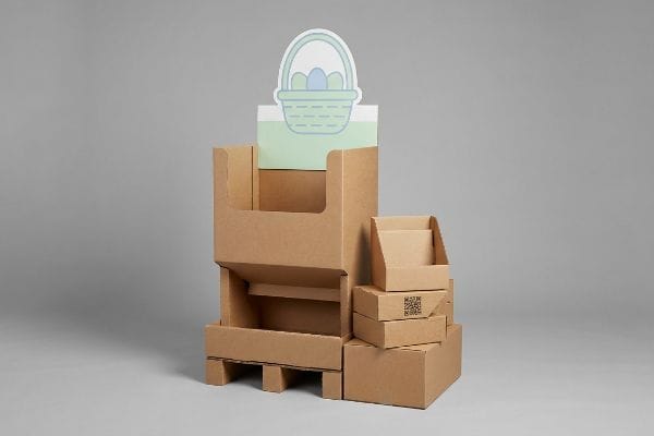 A modular cardboard retail display for Easter, featuring a die-cut header card with an Easter basket and eggs, alongside stacked boxes with a QR code.