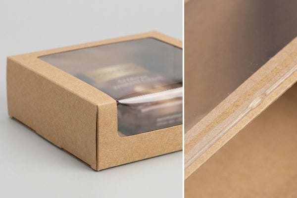Close-up of a brown Kraft paperboard box with a clear plastic window, showcasing the elastic adhesive securing the film to the paper.