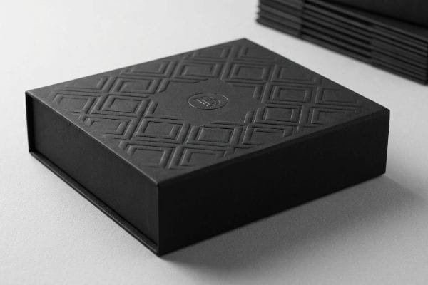 A sleek black luxury box features an embossed geometric pattern and a subtle monogram logo, highlighting premium packaging and luxury printing.