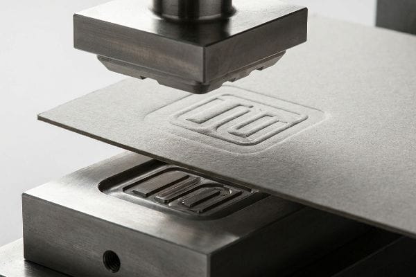 Metal embossing die applying pressure to paperboard, creating a raised tactile pattern on the cellulose fibers.