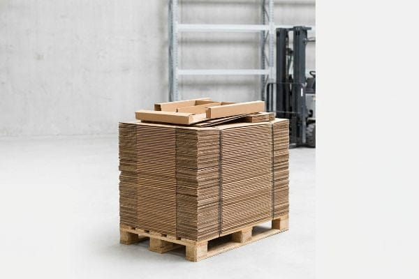 Flat-packed corrugated cardboard sheets stacked on a wooden pallet in a warehouse, ready for efficient shipping and logistics.