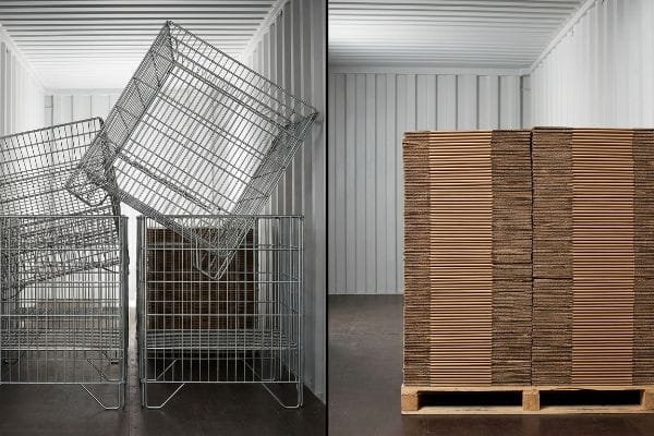 Silver metal wire racks next to stacked flat-pack corrugated cardboard on a pallet in a shipping container.
