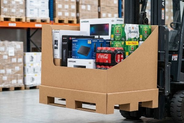 A forklift transports a corrugated pallet display loaded with Samsung electronics, Coca-Cola, Heineken, and Murrells beverages in a warehouse.