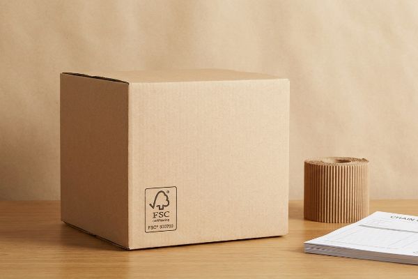 Brown FSC certified corrugated cardboard box with FSC C107010 logo, alongside a roll of packaging material.