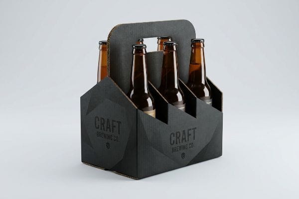 Six amber beer bottles in a black cardboard Craft Brewing Co. six-pack carrier with geometric design.