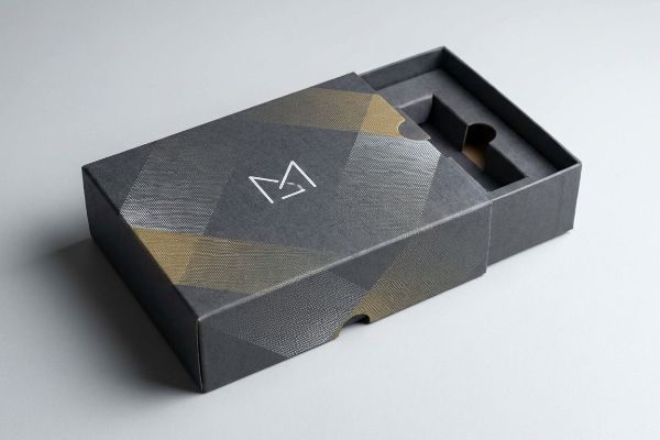 Partially open dark grey custom box featuring a white M logo, gold and silver geometric litho-laminated graphics, and a custom product insert.