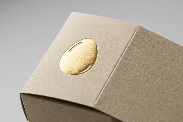 Close-up of a 3D gold embossed egg motif on textured kraft paper packaging, highlighting premium tactile finish.