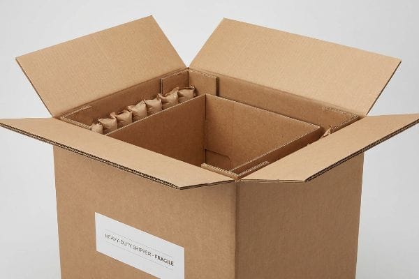 An open heavy-duty corrugated cardboard shipper box with internal dividers and brown paper cushioning, labeled "Heavy-Duty Shipper - Fragile".