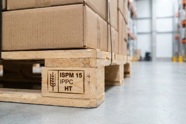 Palette en bois traité thermiquement avec marquage ISPM 15 Ippc Ht supportant des boîtes en carton dans un entrepôt.