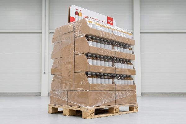 Palletized display of beverage bottles in corrugated trays, shrink-wrapped on a wooden Euro pallet, with 'Produkty Johann Kosian' header.