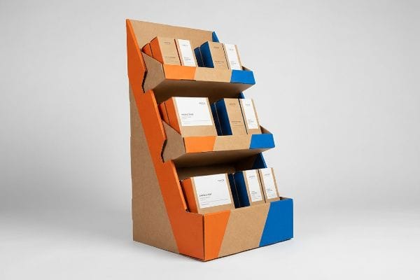 Three-tiered corrugated kraft paperboard POP display with vibrant orange and blue geometric accents, presenting product boxes labeled Vitamin C and Purity & Glow.