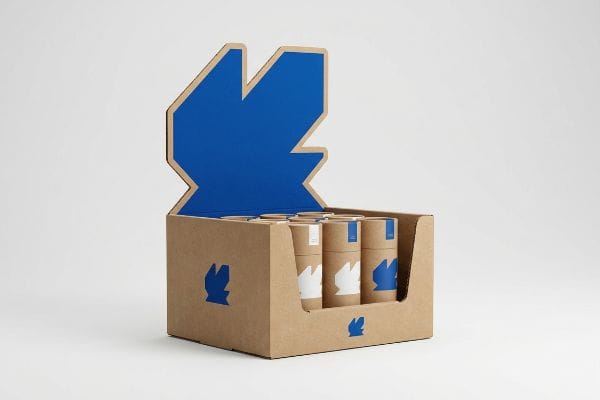 Natural kraft cardboard POP display featuring a blue die-cut header and cylindrical tubes with matching abstract logos.