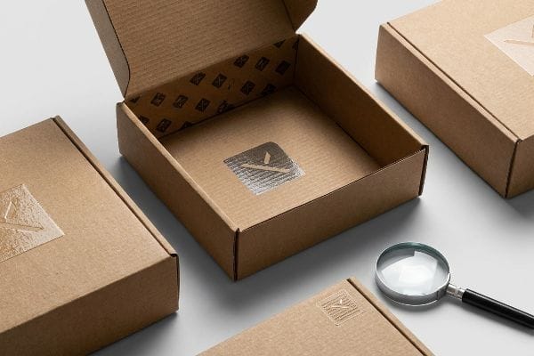 Brown corrugated cardboard boxes with silver foil logos and a magnifying glass, highlighting specialty screen print finishes and tactile textures.