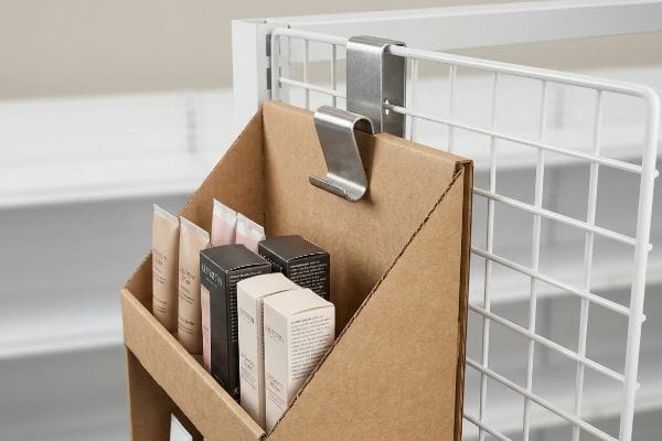 Silver metal S-clip securing a corrugated ARTISAN sidecap display with Creamy Spf 30, Powder Blush, and Perfect Skin products to a white wire rack.
