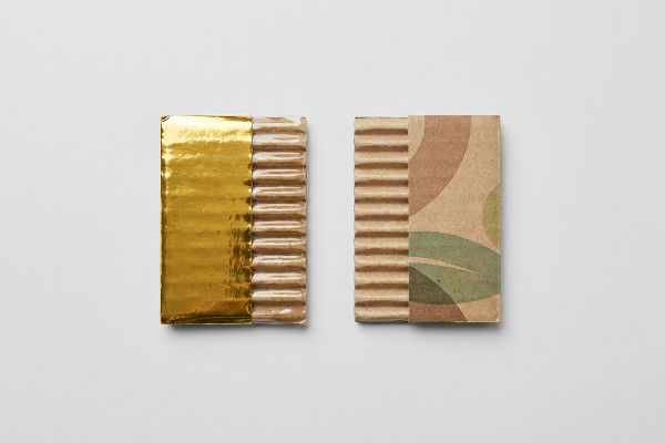Corrugated cardboard samples: one with shiny gold metallic foil, the other with a green and brown leaf print, exposing flutes.