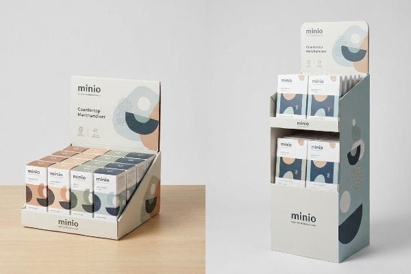 White minio countertop merchandiser displaying product boxes with abstract designs, next to a light blue minio floor stander retail display.