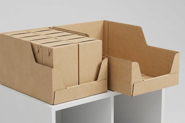 Brown corrugated shelf-ready display trays, one filled with smaller retail boxes, the other empty, on a white shelf.