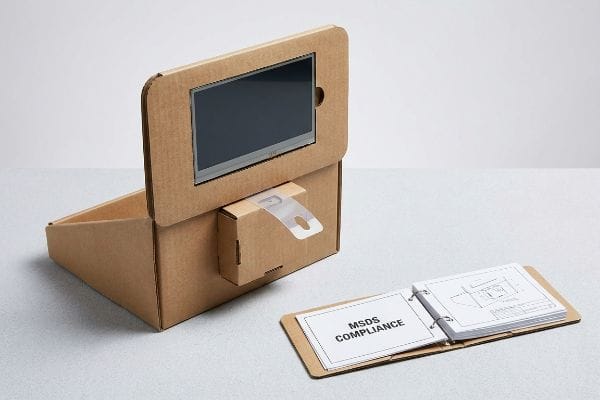 Corrugated cardboard display with embedded digital monitor, a pull-tab battery compartment, and an open Msds Compliance booklet.