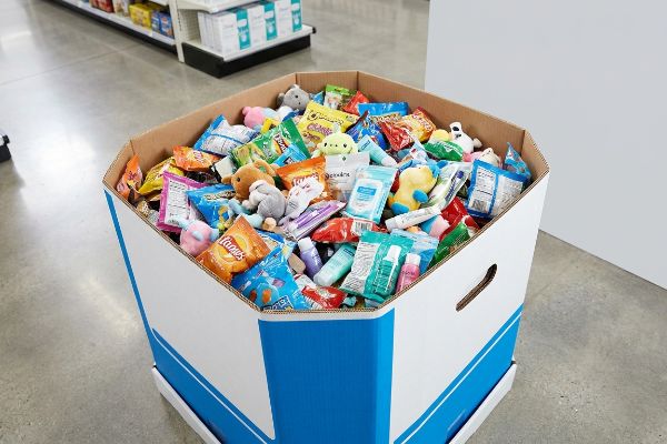 A retail dump bin, white with blue accents, filled with impulse-buy items: plush toys, Fritos snacks, and Good & Gather travel cosmetics.