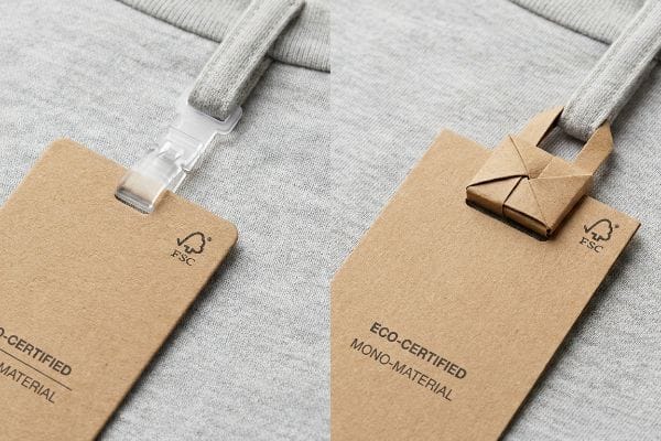 Anhänger aus Kraftpapier mit FSC-Logo, kontrastierend mit einem transparenten Kunststoffclip und einem Papierverschluss im Origami-Stil für Eco-Certified Mono-Material Bekleidung.