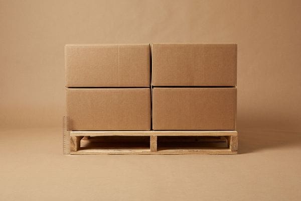 Corrugated master cartons stacked two high on a wooden GMA pallet, with a ruler measuring overhang.