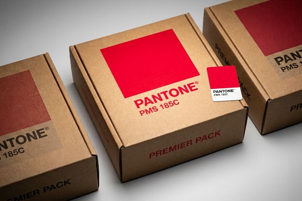 Three brown cardboard boxes display Pantone PMS 185C spot color swatches, with one box featuring a Premier Pack label.