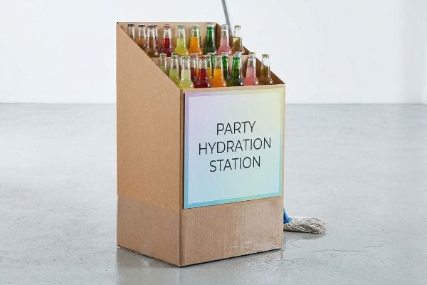 Party Display Moisture Risk Brown corrugated cardboard "Party Hydration Station" display with colorful bottles on a wet floor next to a mop, illustrating moisture risk.