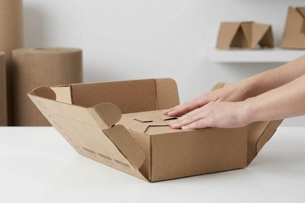 Brown corrugated cardboard PDQ display tray being assembled by hands, showcasing an intuitive auto-bottom design.