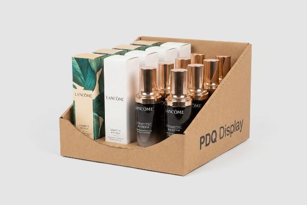 Brown corrugated PDQ display tray with a die-cut swoop, showcasing Lancôme cosmetic serum bottles and boxes.
