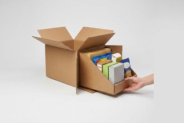 Un présentoir PDQ en carton ondulé brun est extrait d'un carton d'expédition, révélant un plateau modulaire pré-rempli de produits.