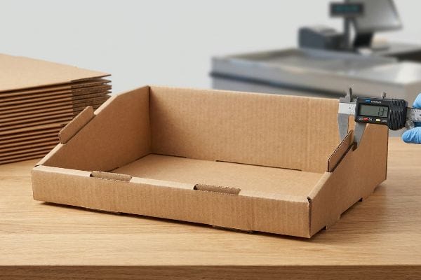 Brown E-flute corrugated cardboard PDQ display tray measured by a digital caliper showing 1.3mm thickness.