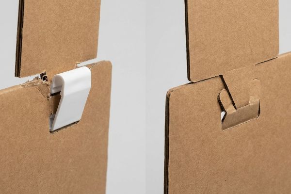 White plastic clip causing edge crushing in corrugated cardboard, contrasted with a precise origami paper lock for display assembly.