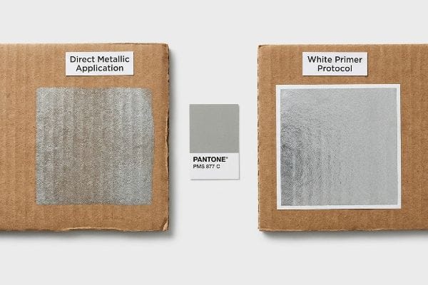 Two corrugated board samples compare Direct Metallic Application and White Primer Protocol for Pantone PMS 877 C silver, showing improved optical gloss with primer.