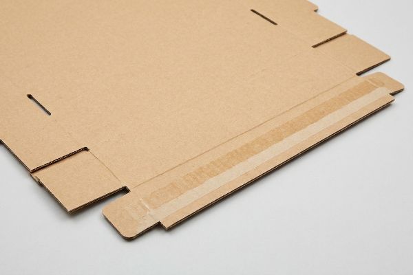 An unfolded brown corrugated PDQ tray displays its pre-glued strip and die-cut slots, highlighting the flat-pack design for efficient assembly.