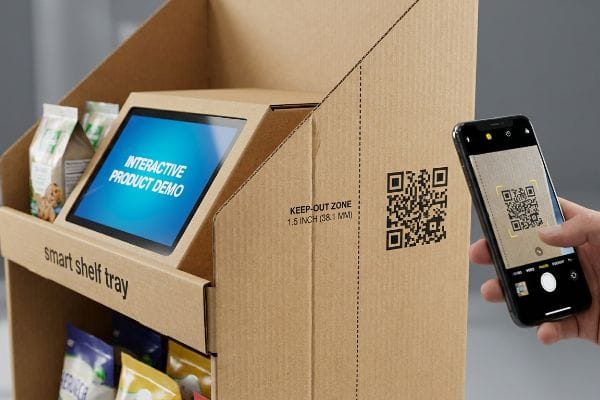 Plateau de rayonnage intelligent en carton ondulé avec « Démo de produit interactive » à l'écran, un smartphone scannant un code QR près de « Zone interdite 1,5 pouce (38,1 mm) ».