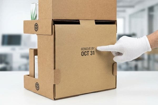 Remove By Date Box Brown corrugated cardboard display box with a gloved hand pointing to "Remove By: Oct 31" date, ensuring timely retail rotation.