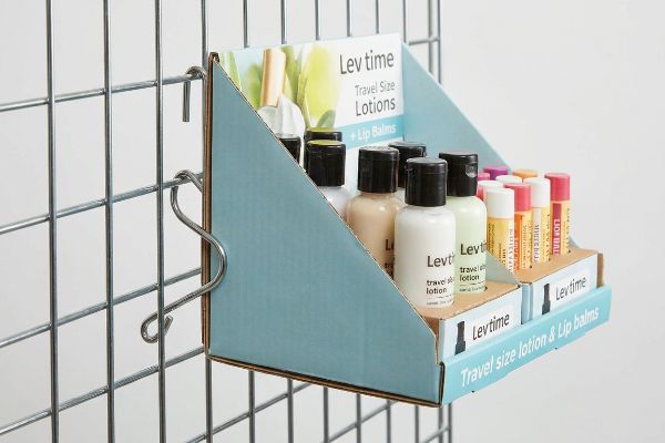 Powder-coated metal S-clip secures a light blue corrugated sidecap display on a wire grid, showcasing Lev time Travel Size Lotions and Lip Balms.