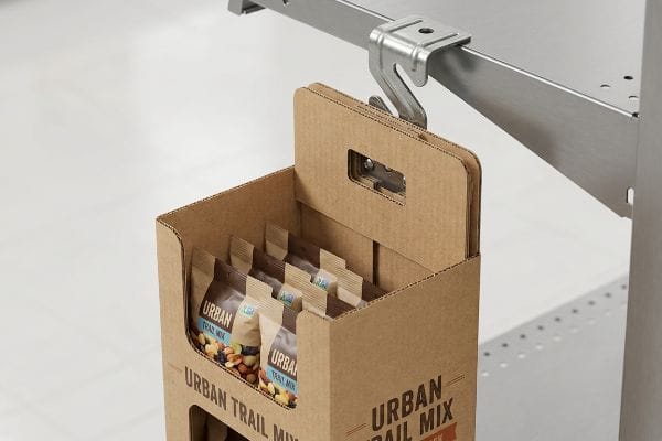 Présentoir latéral en carton ondulé brun contenant des sachets de mélange de fruits secs urbains, fixé par un clip en S métallique universel à une étagère métallique.