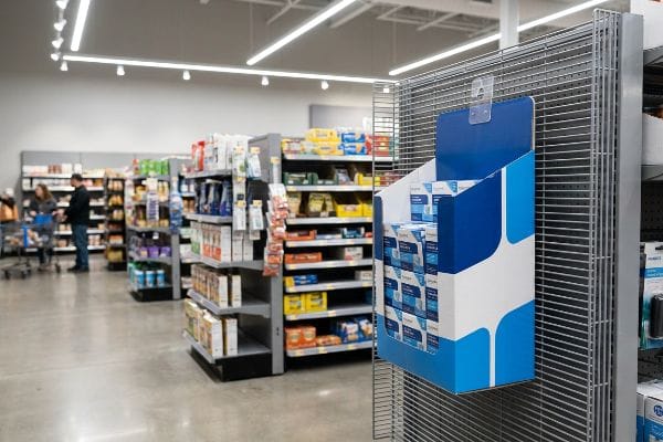 A retail store aisle features a blue and white Similasan sidekick display attached to a metal shelf, maximizing impulse purchases.