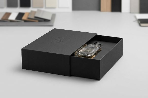 A sleek black rigid box with a sliding drawer reveals a clear glass perfume bottle, featuring a subtle embossed logo on the lid.