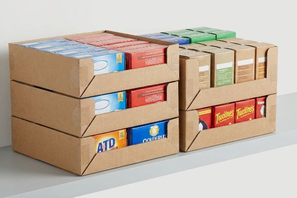 Two stacks of brown cardboard stackable PDQ trays filled with Atd, Goldenleaf, and Twinings product boxes for retail display.