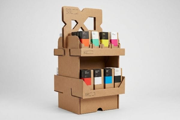 Natural corrugated cardboard POP display features a stylized logo die-cut header and two tiers of high-contrast colorful product boxes, showcasing asymmetrical SKU spacing.