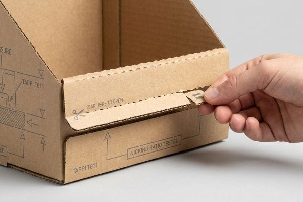 Corrugated box tear-away perforation being pulled, showing 'Tear Here To Open', 'Tappi T811', 'Nicking Ratio Tested'.