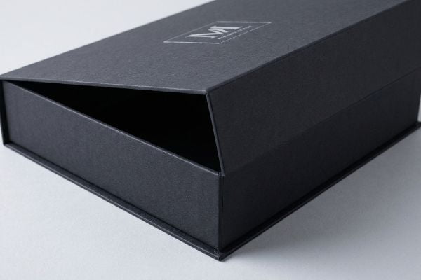 Textured black luxury packaging box with a partially open lid, featuring a silver foil VM Monterra logo.