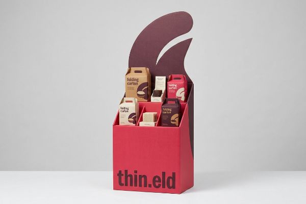 Vibrant red Thin.eld visual merchandising display with a die-cut maroon header, showcasing 'folding carton' products.