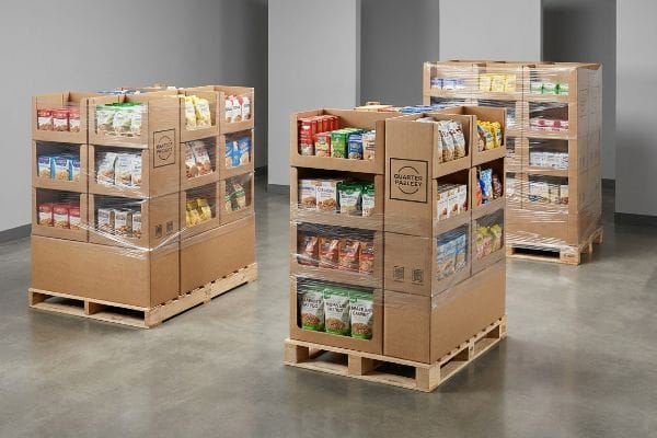 Shrink-wrapped cardboard Quarter Pallet displays, filled with diverse snack products, on wooden bases, ready for retail placement.